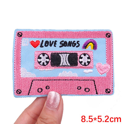 Pink cassette tape patch with 'Love Songs' text held by a hand on a white background