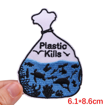 Embroidered patch of a plastic bag with 'Plastic Kills' text and underwater scene, held by a hand.
