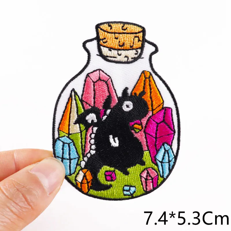 Embroidered patch of a black cat in a bottle with colorful crystals held by a hand.