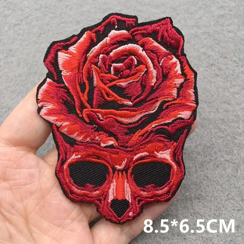 Red rose and skull design patch held by a hand on a gray background