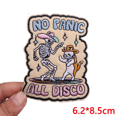 Embroidered patch with skeleton and cat dancing, text 'No Panic All Disco', held by a hand.