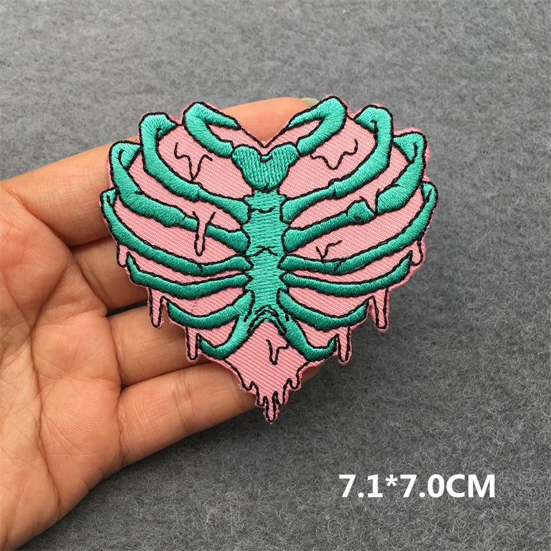 Heart-shaped patch with green skeleton design held by a hand on a gray background