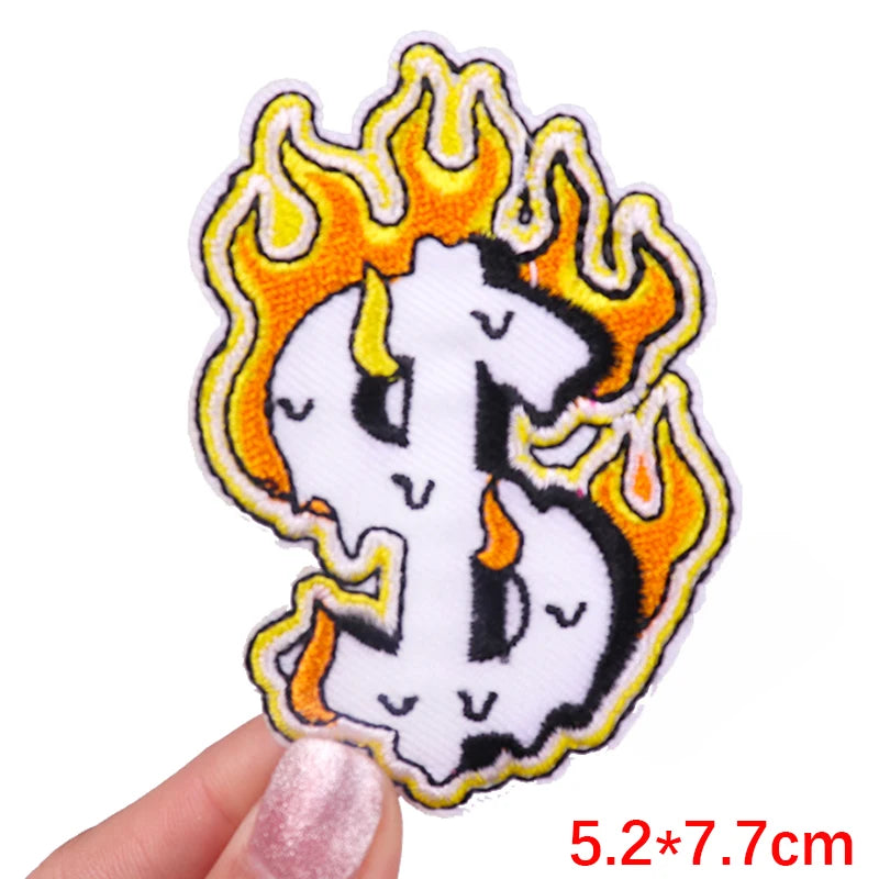 Flame-themed dollar sign patch held by a finger with measurement text on a white background