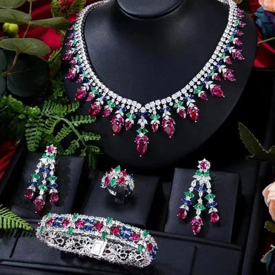 Jewelry set with necklace, earrings, ring and bracelet on a black stand with green leaves in the background.