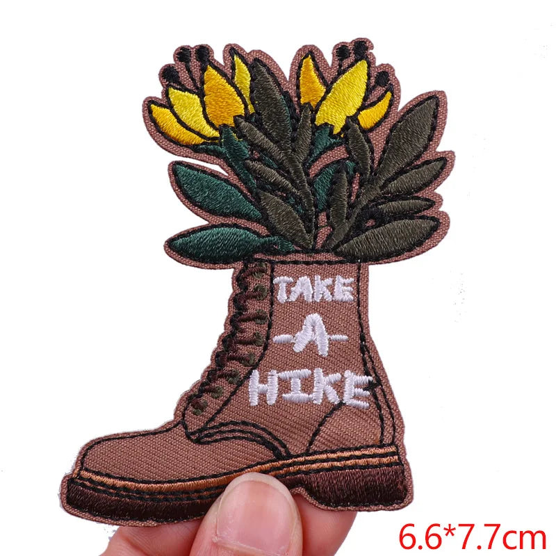 Embroidered patch of a boot with flowers and 'Take a Hike' text, held by a hand.