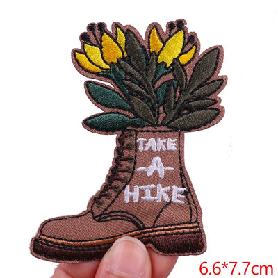 Embroidered patch of a boot with flowers and 'Take a Hike' text on a white background