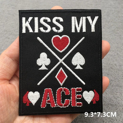 Patch with 'Kiss My Ace' text and card suit symbols held by a hand on a gray background.