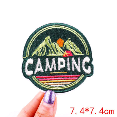 Camping-themed patch held by a hand with glittery nail polish on a white background.