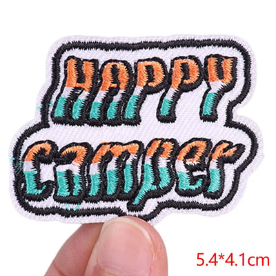 Embroidered patch with 'Happy Camper' text held by a hand, with dimensions displayed.