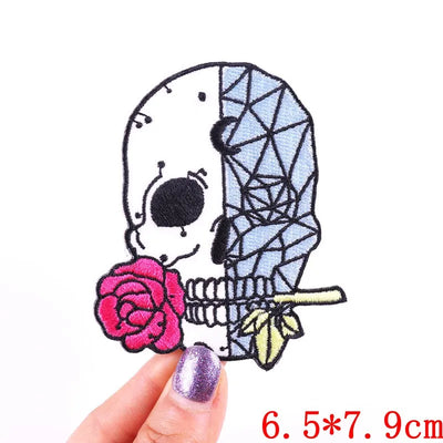Embroidered patch of a skeleton holding a rose, held by a hand with purple nail polish on a white background.