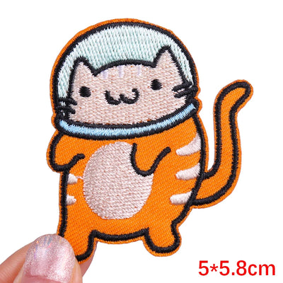 Embroidered patch of a cat in an astronaut suit held by a hand with glittery nail polish.