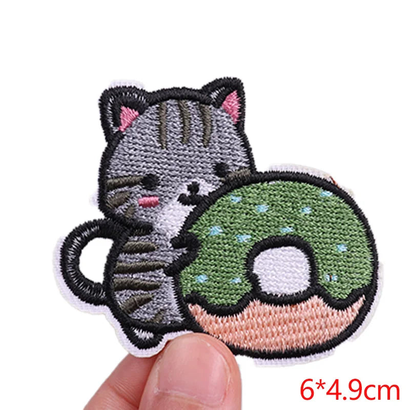 Embroidered patch of a cat holding a green donut with a hand holding it on a white background.