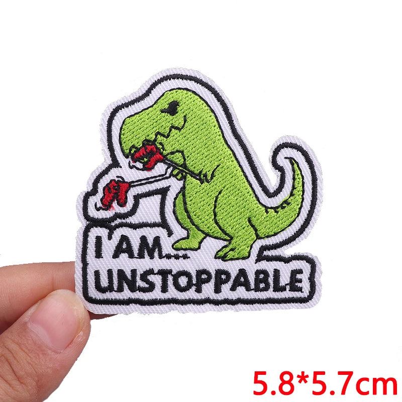 Embroidered patch with a dinosaur and 'I am unstoppable' text held by a hand on a white background.