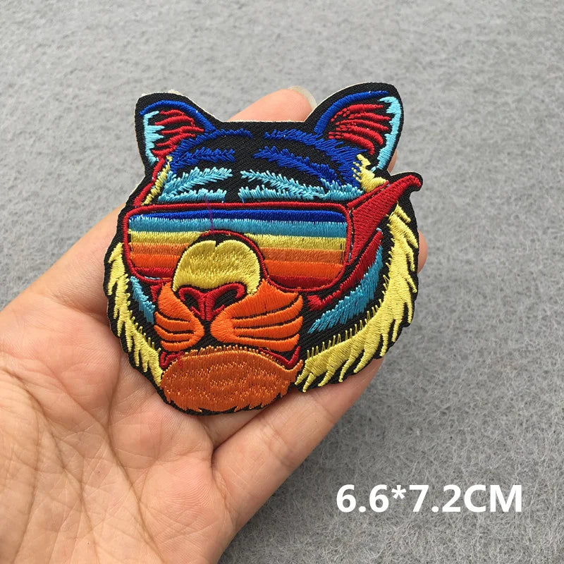 Colorful embroidered patch of a cat's face held in a hand on a gray background