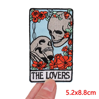 Patch with skeletons and flowers labeled 'The Lovers' held by a hand.