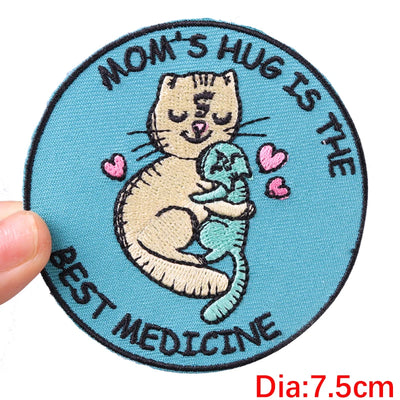 Circular patch with a cat illustration and text 'Mom's hug is the best medicine' on a blue background.
