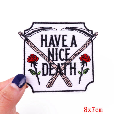Embroidered patch with 'Have a Nice Death' text and roses, held by a hand.