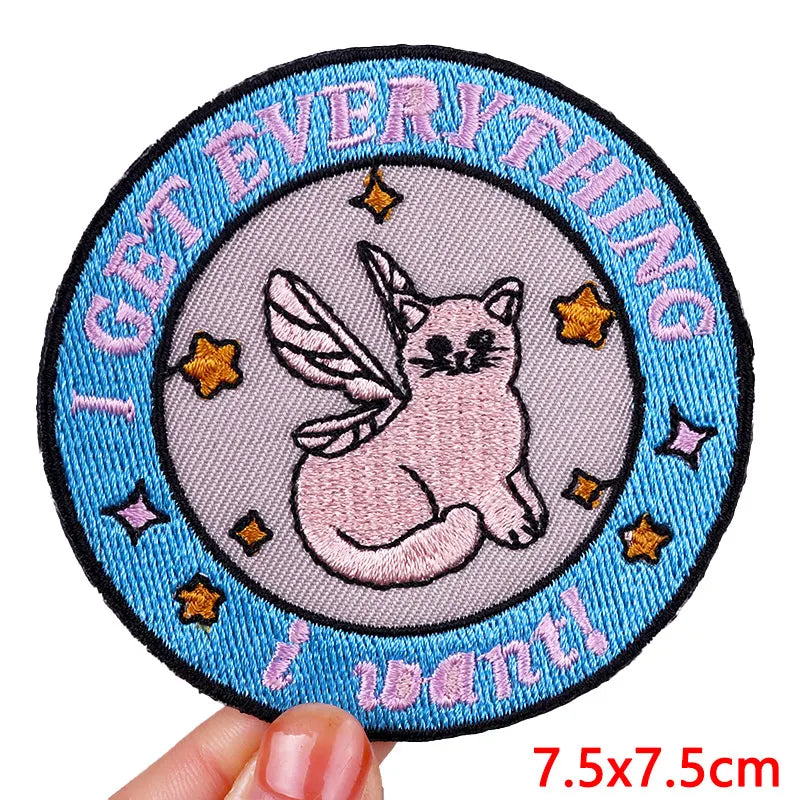 Circular patch with a cat unicorn design and text 'I get everything I want' held by a hand.