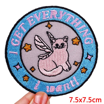 Circular patch with a cat unicorn design and text 'I get everything I want' held by a hand.