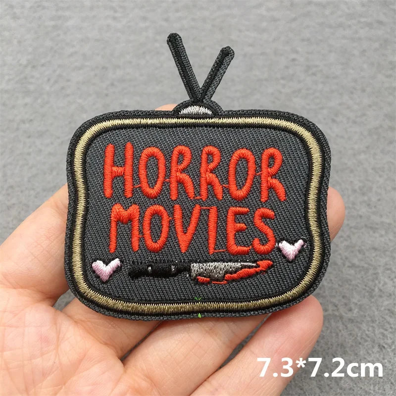 Patch with 'Horror Movies' text held in a hand against a gray background