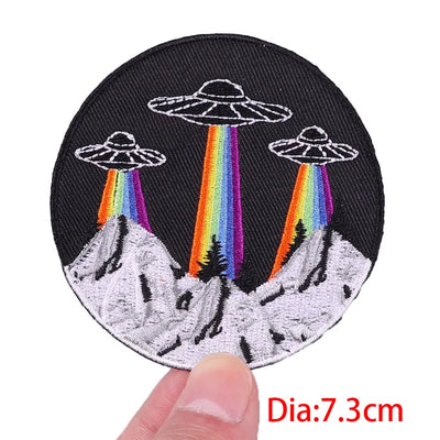 Circular patch with UFOs and rainbows held by a hand, labeled 'Dia:7.3cm'.