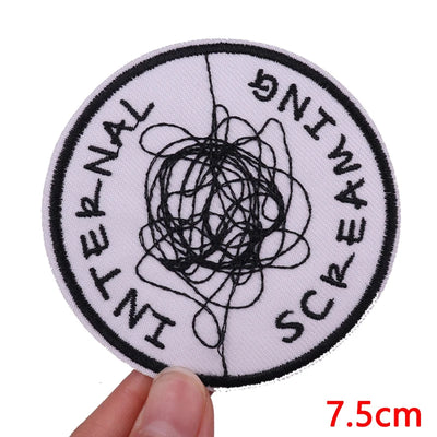 Circular patch with black scribble and text held by a hand, on a white background.