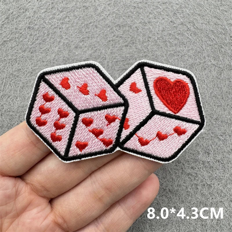 Two pink dice-shaped patches with red hearts on a gray background