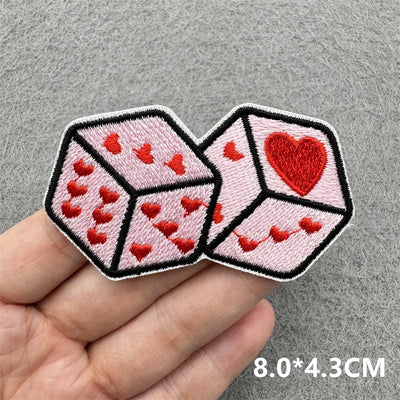 Two pink dice-shaped patches with red hearts on a gray background