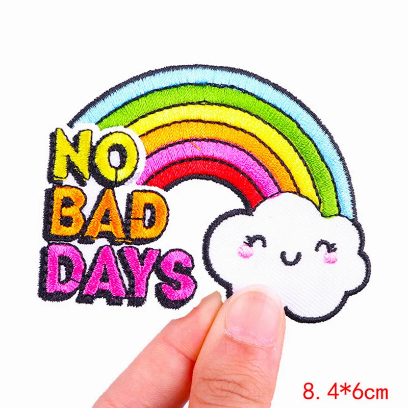 Embroidered patch with rainbow and cloud design and 'No Bad Days' text, held by a hand.