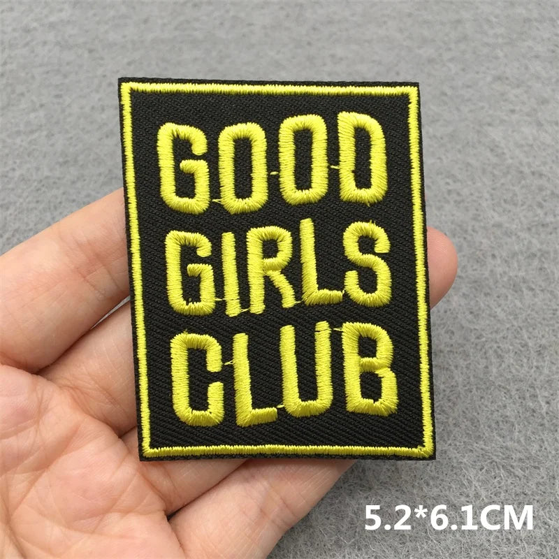 Patch with 'GOOD GIRLS CLUB' text held by a hand on a gray background