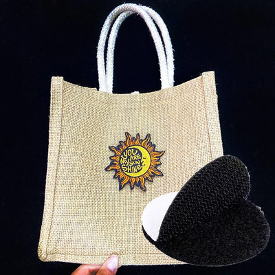 Jute bag with a sun design and text, held by a hand against a black background
