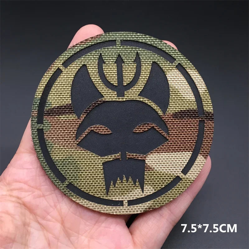 Circular metal badge with black symbol held in a hand against a dark background