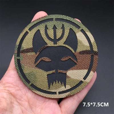 Circular metal badge with black symbol held in a hand against a dark background