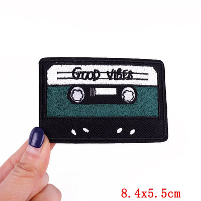 Cassette tape-shaped patch with 'Good Vibes' text held by a hand on a white background