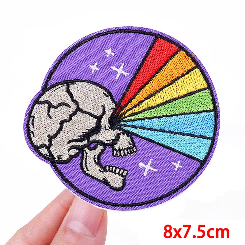 Circular patch with skull and rainbow design held by a hand, on a white background.
