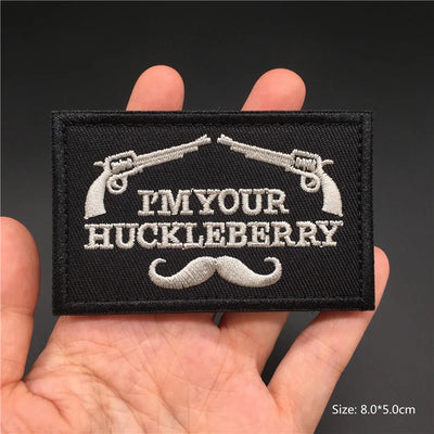 Embroidered patch with 'I'm your Huckleberry' text and revolvers held in hand against a dark background