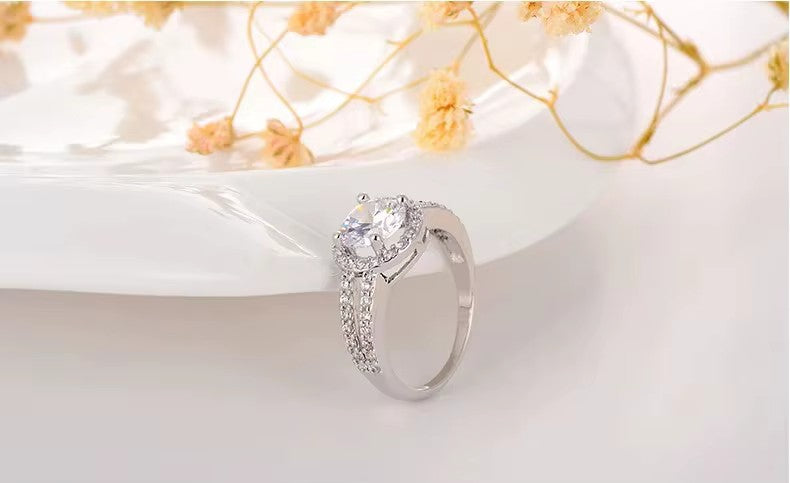 Silver ring with a large central crystal and smaller crystal on a white surface with yellow flowers.