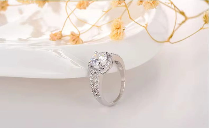 Silver ring with a large central crystal and smaller crystal on a white surface with yellow flowers.