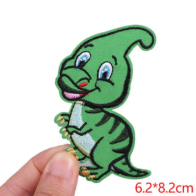 Green cartoon dinosaur patch held by a hand with size measurement on a white background