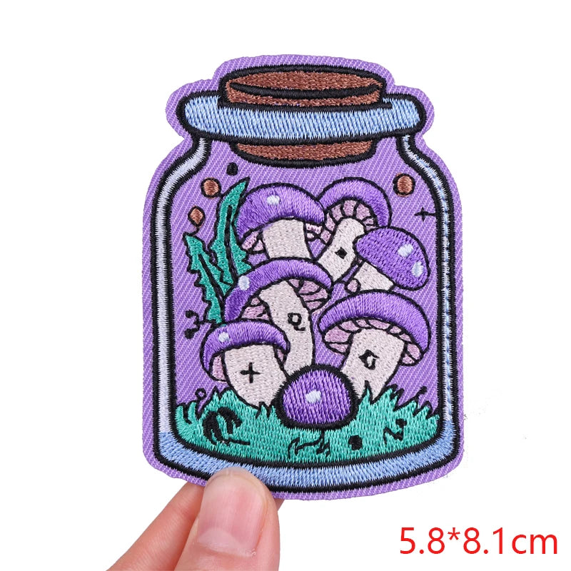 Embroidered patch of mushrooms in a jar held by a hand on a white background