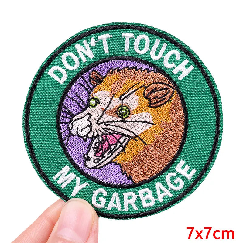 Embroidered patch with a fox design and text 'Don't Touch My Garbage' held by a hand.