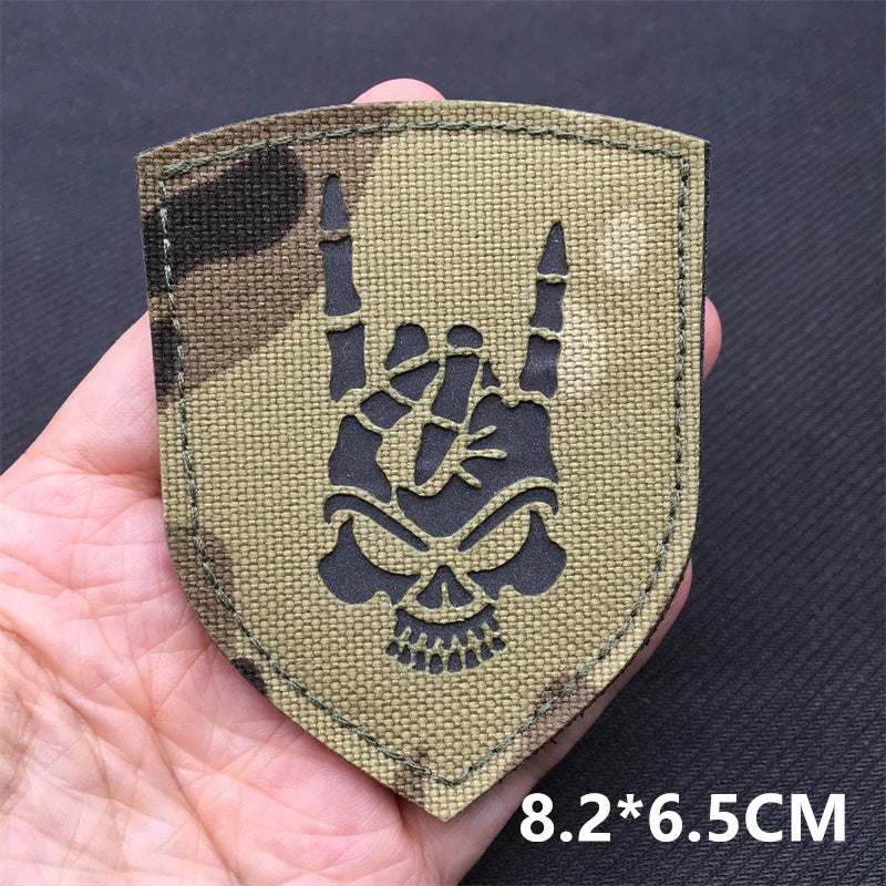 Tactical patch with skull and hand gesture design held in a hand against a dark background