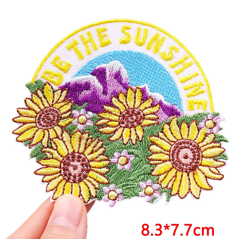 Embroidered patch with sunflowers and 'Be the Sunshine' text held by a hand.