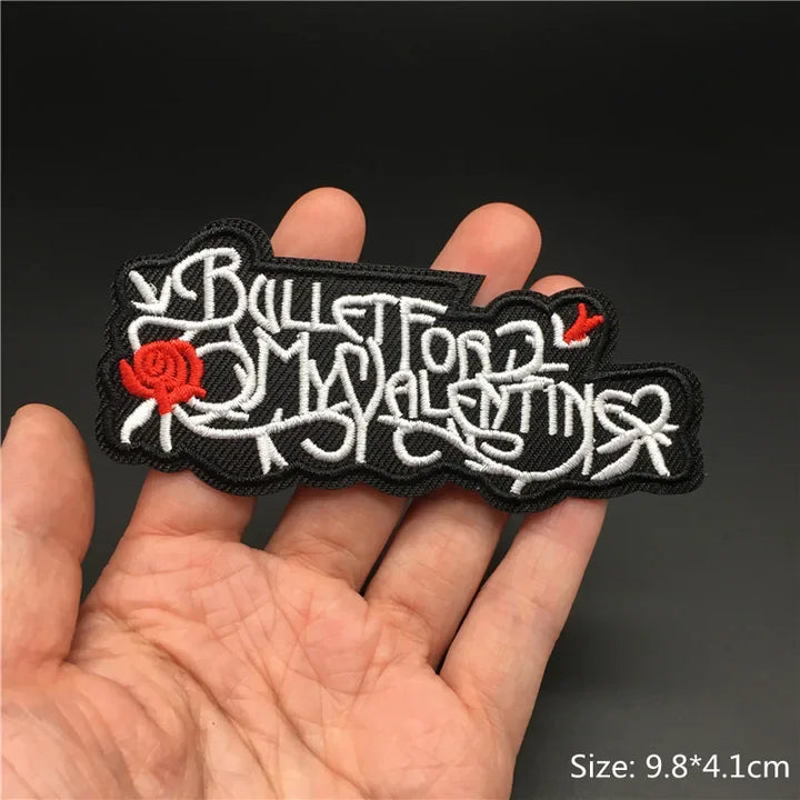 Hand holding a black white and red Bullet For My Valentine embroidered iron-on patch 9.8x4.1cm on a dark background