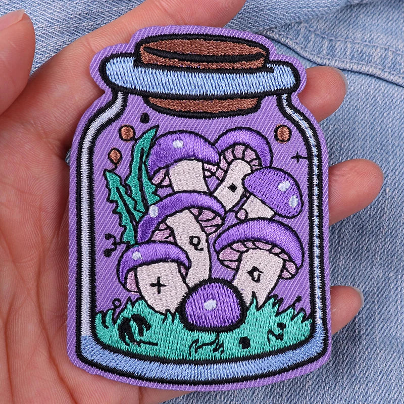 Embroidered patch of mushrooms in a jar held in a hand against a denim background