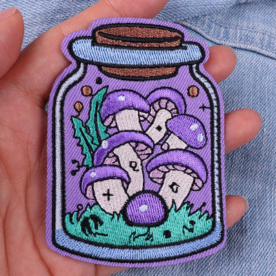 Embroidered patch of mushrooms in a jar held in a hand against a denim background