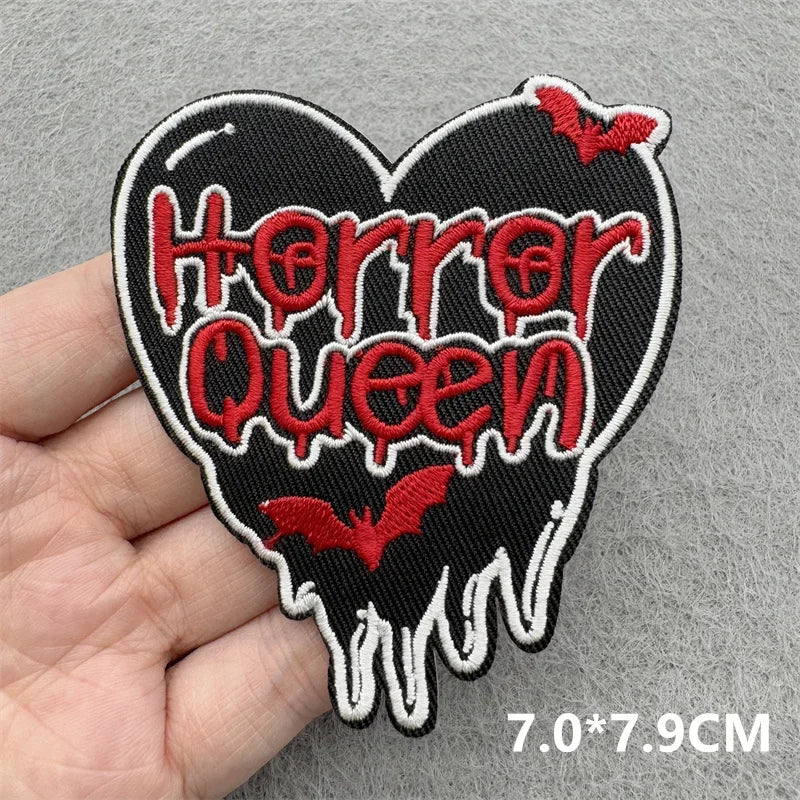 Heart-shaped patch with 'Horror Queen' text held by a hand on a gray background