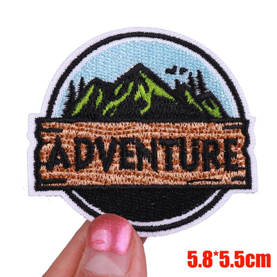Patch with mountain design and 'ADVENTURE' text held by a hand on a white background
