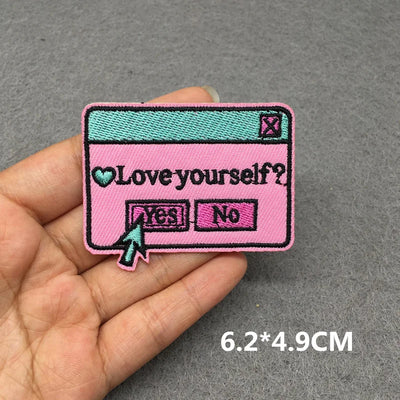 Pink patch with 'Love yourself?' question and 'YES'/'NO' buttons held in a hand on a gray background.