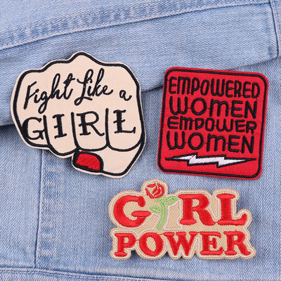 Three motivational patches on a denim background: 'Fight Like a Girl', 'Empowered Women Empower Women', and 'Girl Power'.